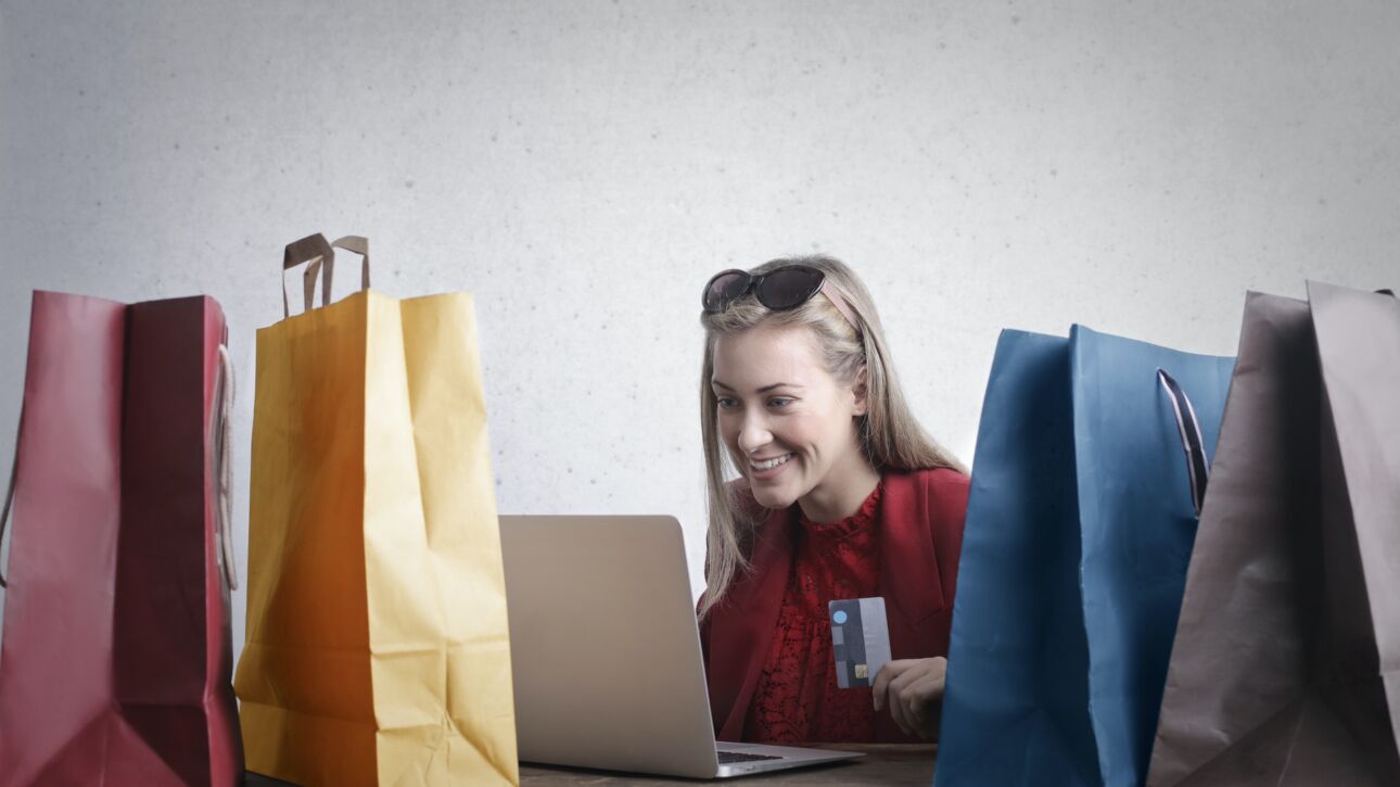 blonde female customer looking at a laptop surrounded by shopping bags and holding a credit card