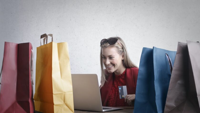 blonde female customer looking at a laptop surrounded by shopping bags and holding a credit card