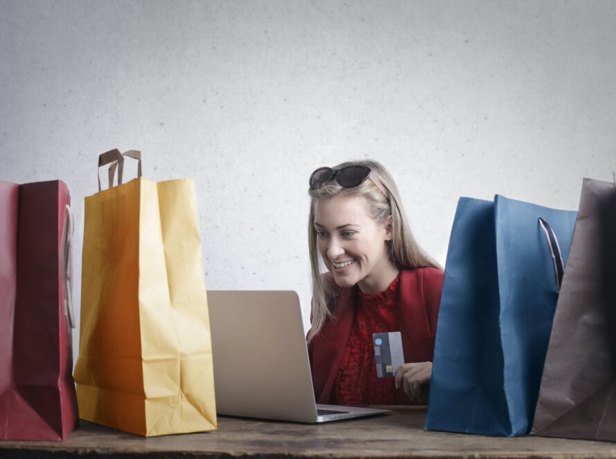 blonde female customer looking at a laptop surrounded by shopping bags and holding a credit card
