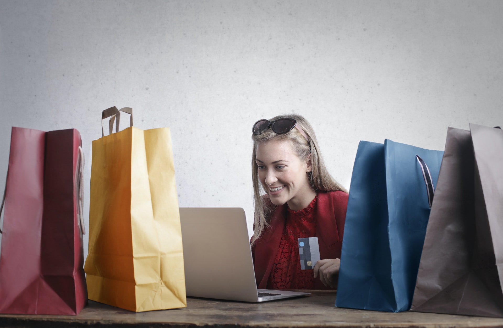 blonde female customer looking at a laptop surrounded by shopping bags and holding a credit card