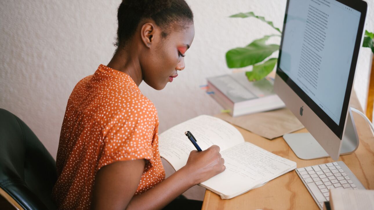 african american female writing relevant content in front of a computer