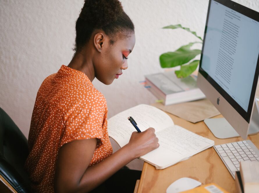 african american female writing relevant content in front of a computer