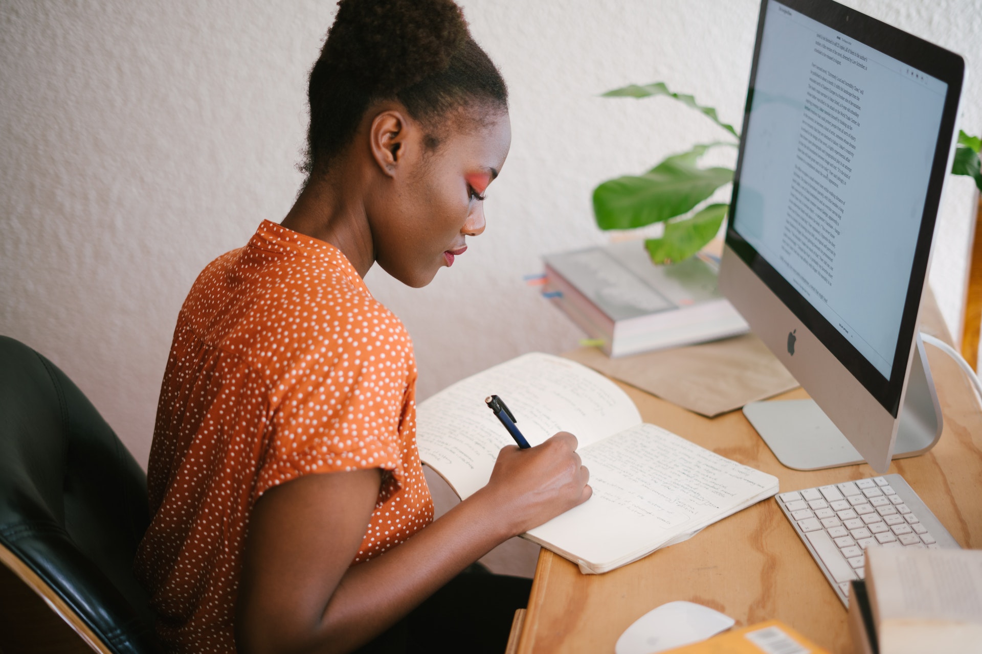 african american female writing relevant content in front of a computer